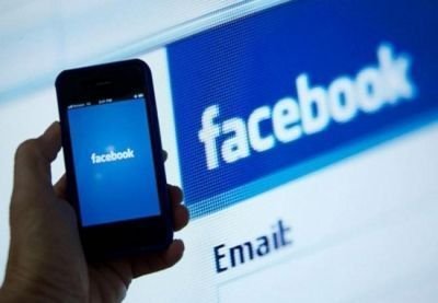 Un usuario accede a Facebook desde su teléfono, con una pantalla con el login detras. AFP